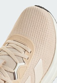 Chaussure de sport beige clair avec une tige en maille texturée, des lacets plats et une semelle rembourrée avec un accent noir contrastant.
