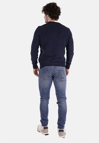 Maglione navy a maglia con polsini e orlo a coste, abbinato a jeans azzurri chiari e sneakers bianche, visto da dietro.