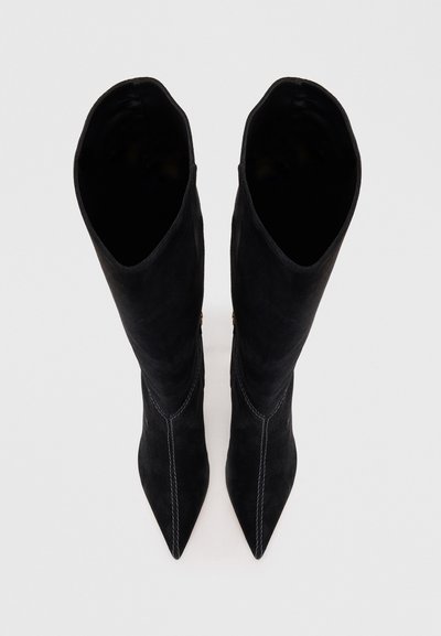 Μαύρες σουέτ μπότες μέχρι το γόνατο με μυτερή μύτη, που διαθέτουν αντίθετη ραφή και λεία εσωτερική επένδυση. Χωρίς ορατό υλικό ή διακοσμητικά στοιχεία.