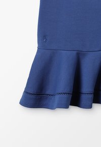 Navyblaues Kleid mit ausgestelltem Saum, ausgestattet mit einem strukturierten Stoff, Spitzenverzierungen am Saum und einem kleinen gestickten Logo in der Nähe der Taille.