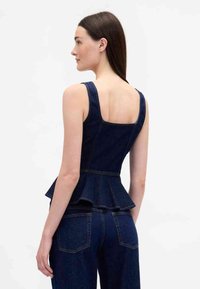 Tume denimist peplum-tüüp ülaosa ruudukujulise seljaga, laiad rihmad, kontrastõmblused ja lehviku kujuline ääreosa. Modell kannab kokku sobivaid denimist pükse.