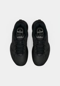 Par de ténis Air Monarch pretos com atacadores, colarinhos acolchoados e palmilhas visíveis rotuladas com o tamanho "D" e marca.