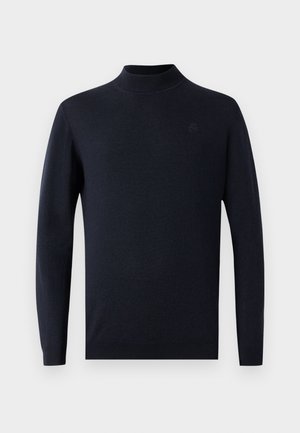 Tummansininen neulottu neulepaita, jossa on korkea kaulus ja pitkät hihat. Materiaali vaikuttaa sileältä, ja rinnassa on hienovarainen logodetail.