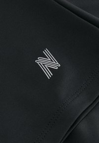 Zwarte sportstof met een verhoogde textuur en een opvallend grijs "N"-logo. De stiksels zijn netjes, wat de kwaliteit van het vakmanschap benadrukt.