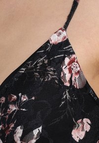 Schwarzer Spitzenstoff mit floralen Mustern in Pink und Weiß; weist dünne Träger und eine zarte Textur auf, die die Blumenmuster deutlich hervorhebt.