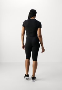 Conjunto atlético negro, con una blusa de manga corta y pantalones cortos hasta la rodilla, confeccionado en tela elástica. Presenta un diseño ajustado y una textura suave.
