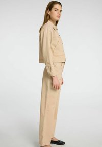 Veste en velours côtelé beige avec des boutons sur le devant et des poches latérales, assortie à un pantalon large, présentant une texture lisse et un design minimal.