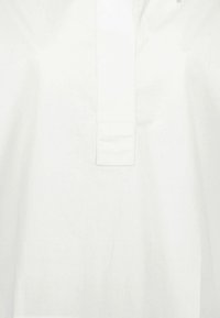 Camicia bianca con bottoni, in cotone, dalla texture morbida, con mezza abbottonatura, maniche corte e superficie liscia e priva di decorazioni.