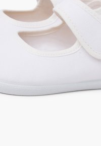 Weißer Schuh aus Stoff mit runden Ausschnitten an den Seiten, glatter Oberfläche, weicher, strukturierter Sohle und einem Klettverschluss für sicheren Halt.