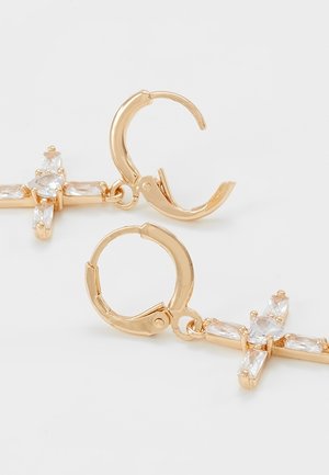 Złote kolczyki koła z wiszącymi krzyżowymi zawieszkami ozdobionymi przejrzystymi, prostokątnymi i okrągłymi kamieniami szlachetnymi na białym tle.