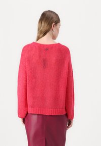 Pull en tricot rose vif avec une coupe ample, des épaules tombantes et un ourlet côtelé. Dispose d'un détail de bouton dans le dos pour une touche de style supplémentaire.