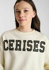 Crèmekleurige crewneck sweatshirt met opvallende "CERISES" lettering in zwart met een textuur van dierenprint. Zacht materiaal, relaxte pasvorm.