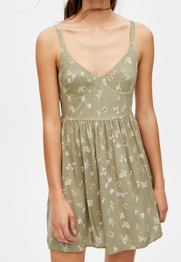 Robe florale verte avec des bretelles fines, un décolleté en V, un corsage ajusté et une jupe évasée ; présente de petits motifs de fleurs et de feuilles.