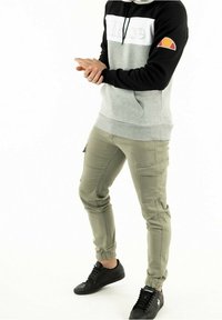 Sudadera con capucha gris y negra con un logo, combinada con pantalones cargo verde oliva y zapatillas negras. Características incluyen puños elásticos y bolsillos laterales.