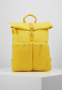 Mochila amarilla hecha de tela texturizada con tapa plegable, cremallera plateada, bolsillos de malla en la parte frontal y un asa en la parte superior para llevar.