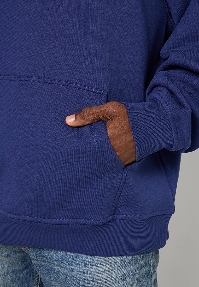 Granatowy hoodie wykonany z miękkiego materiału, z kieszenią kangurzą. Żebrowane mankiety i dół zapewniają dopasowany krój. Tekstura jest gładka.
