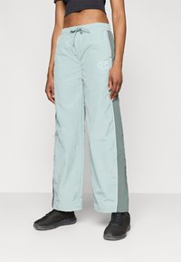 Šviesiai žali, plačių kojų kelnės, pagamintos iš tekstūruotos, lengvos medžiagos, su raišteliu reguliuojamu juosmeniu ir baltais šonų dryžiais bei logotipu.