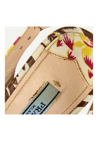 Gros plan d’une semelle intérieure en cuir beige avec un bord en tissu montrant un motif floral coloré et une étiquette visible à l’intérieur de la chaussure.