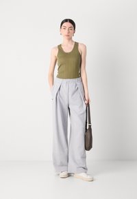 Olivengrønn ribbet tank topp, grå vide joggebukser, hvite sneakers og en liten brun skulderveske. Minimalistisk design med folder.