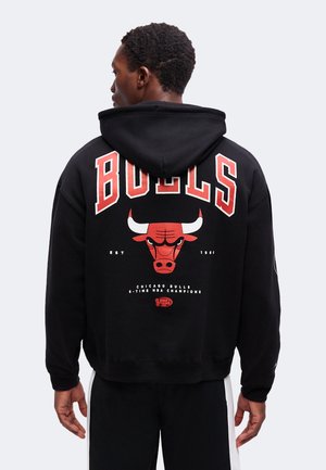Άτομο που φοράει μαύρο φούτερ Chicago Bulls, δείχνοντας την πλάτη με το κόκκινο λογότυπο ταύρου και κείμενο που υπογραμμίζει την ομάδα και τα χρόνια πρωταθλήματος.