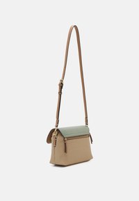 Sac à bandoulière avec un corps tressé beige, un rabat texturé vert, une poche zippée à l'avant et une bandoulière en cuir brun clair réglable avec une quincaillerie dorée.