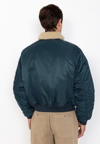Marineblauwe bomberjack met een pluizige beige kraag, geribbelde zoom en elastische manchetten. Kenmerkt zich door een gladde, glanzende textuur en gevoerde schouders.