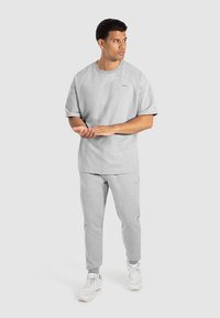 Szary zestaw bluzy i spodni dresowych wykonany z miękkiego materiału. T-shirt ma krótkie rękawy i luźny krój, spodnie są zwężane.