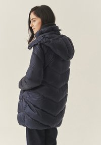 Mornarica jakna s kapuljačom, s quilted dizajnom, visokim ovratnikom i opuštenim fitom, izrađena od laganog, vodootpornog materijala.