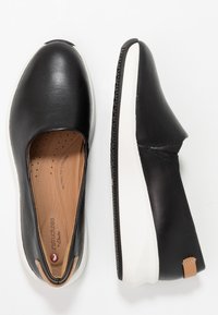 Chaussures noires en cuir à enfiler avec une semelle blanche, bout arrondi et rembourrage intérieur. Présente une accentuation brun clair au talon.