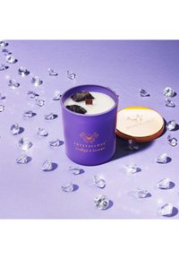 Fioletowy słoik na świeczkę z białym woskiem, zawierający kryształy ametystu i brązowy akcent. Złota nakrętka obok słoika, na jasnofioletowym tle z przezroczystymi kamieniami.