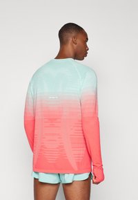 Lange mouw atletisch shirt in een verlopen mint naar koraal, met textuurpatronen en duimgaten, gecombineerd met bijpassende mintkleurige shorts.
