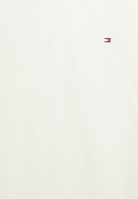 Vit bomull T-shirt med en liten broderad logotyp i rött, blått och vitt. Mjuk textur och enkel design utan ytterligare mönster.