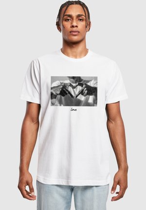 White cotton t-shirt featuring a black and white graphic of hands forming a heart shape, with the word "love" printed below.