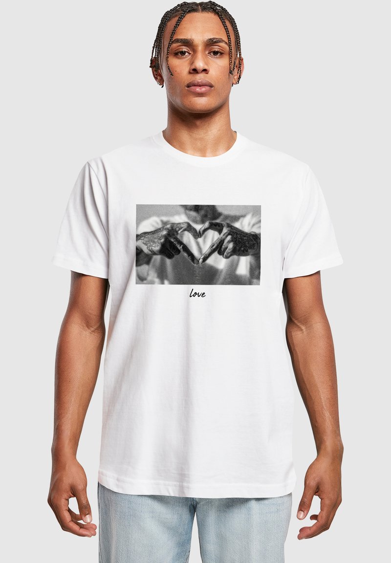 Hvid bomulds t-shirt med et sort-hvidt grafik af hænder, der danner et hjerte, med ordet "kærlighed" trykt nedenunder.