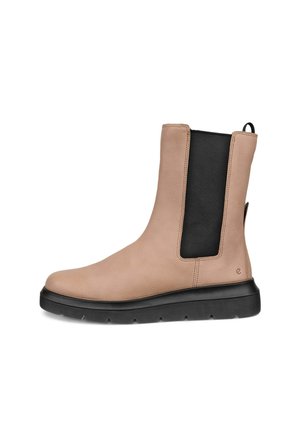 Botte cheville en cuir tan avec panneaux élastiques noirs sur les côtés, bout rond et semelle en caoutchouc noir. Elle est dotée d'une languette à l'arrière.