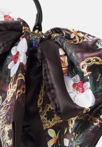 Écharpe en soie noire avec un motif floral d'orchidées et de chaînes. Texture glossy remarquable et couleurs vives, y compris des détails blancs et rouges.