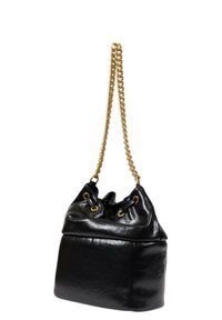 Borsa a secchiello in pelle nera con manico a catena dorata, apertura arricciata e occhielli in ottone. Texture liscia con una base strutturata.