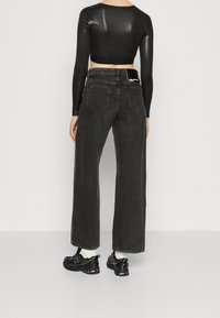 Musta, napakka pitkähihainen crop-top, joka on yhdistetty korkeavyötäröisiin, leveälahkeisiin harmaisiin farkkuihin, joissa on takataskut ja merkkilippu vyötärönauhassa.