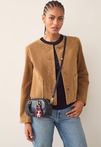 Suèdebruine jas met een ronde halslijn en knopen aan de voorkant; gecombineerd met een zwarte tas met een kleurrijke hanger, gedragen met blauwe spijkerbroek.