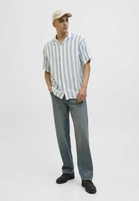 Chemise à manches courtes avec des boutons en tissu léger, ornée de rayures bleues, associée à un jean bleu ample et des chaussures noires, complétée par une casquette beige.