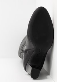 Bottine en cuir noir avec fermeture éclair latérale, semelle inclinée vers l'avant affichant la taille 37 et le nom de la marque Unisa sur la semelle.