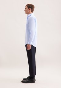 Camicia azzurra a maniche lunghe con tasca, abbinata a pantaloni scuri e scarpe nere. Tessuto morbido e vestibilità su misura.