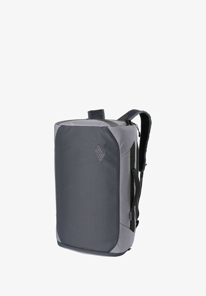Sac à dos rectangulaire gris et noir avec bretelles rembourrées, poignée latérale et poche avant zippée, affichant le logo de la marque Nitro.