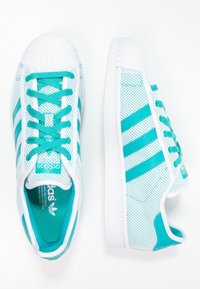 Ett par vita sneakers med turkosa ränder och snöre, en sko vänd uppåt och den andra som visar yttersidan.