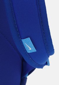 Kék hátizsák texturált anyaggal, párnázott pántokkal és egy kis világoskék Nike logóval. Kényelmes és tartós használatra tervezve.