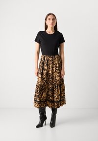 Top in maglia nera con gonna fluida a stampa leopardo, caratterizzata da un design a strati e rifiniture a contrasto. Abbinata a stivali neri al ginocchio.