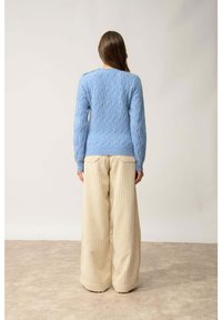 Jasnoniebieski sweter z warkoczowym splotem i długimi rękawami, w połączeniu z szerokimi, beżowymi spodniami z prążkowanej tkaniny. Teksturowany materiał o luźnym kroju.