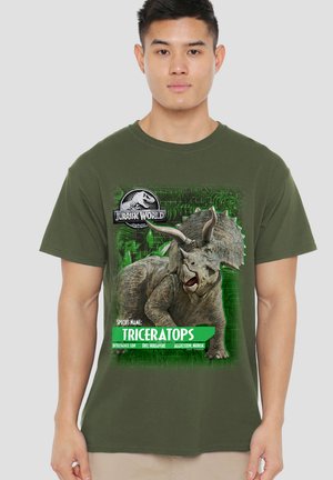 Junger Mann mit grünem Jurassic World T-Shirt zeigt eine Illustration eines Triceratops-Dinosauriers und Angaben zur Art.