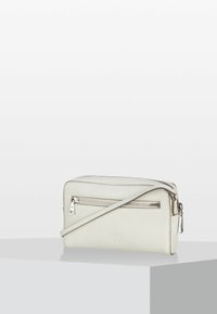 Bílá kožená kabelka přes rameno s texturovaným povrchem, zipovými přihrádkami a odnímatelným popruhem. V přední části má jemně embosované logo.