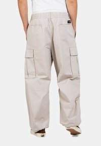 Helle beige Cargo-Hosen mit elastischem Bund, mehreren Seitentaschen und einer lockeren Passform. Der Stoff scheint glatt zu sein mit minimalen Texturdetails.